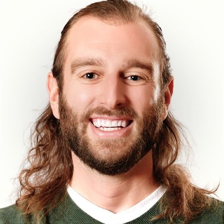 Bill Yost, smiling, with long hair and a beard, in a green sweater